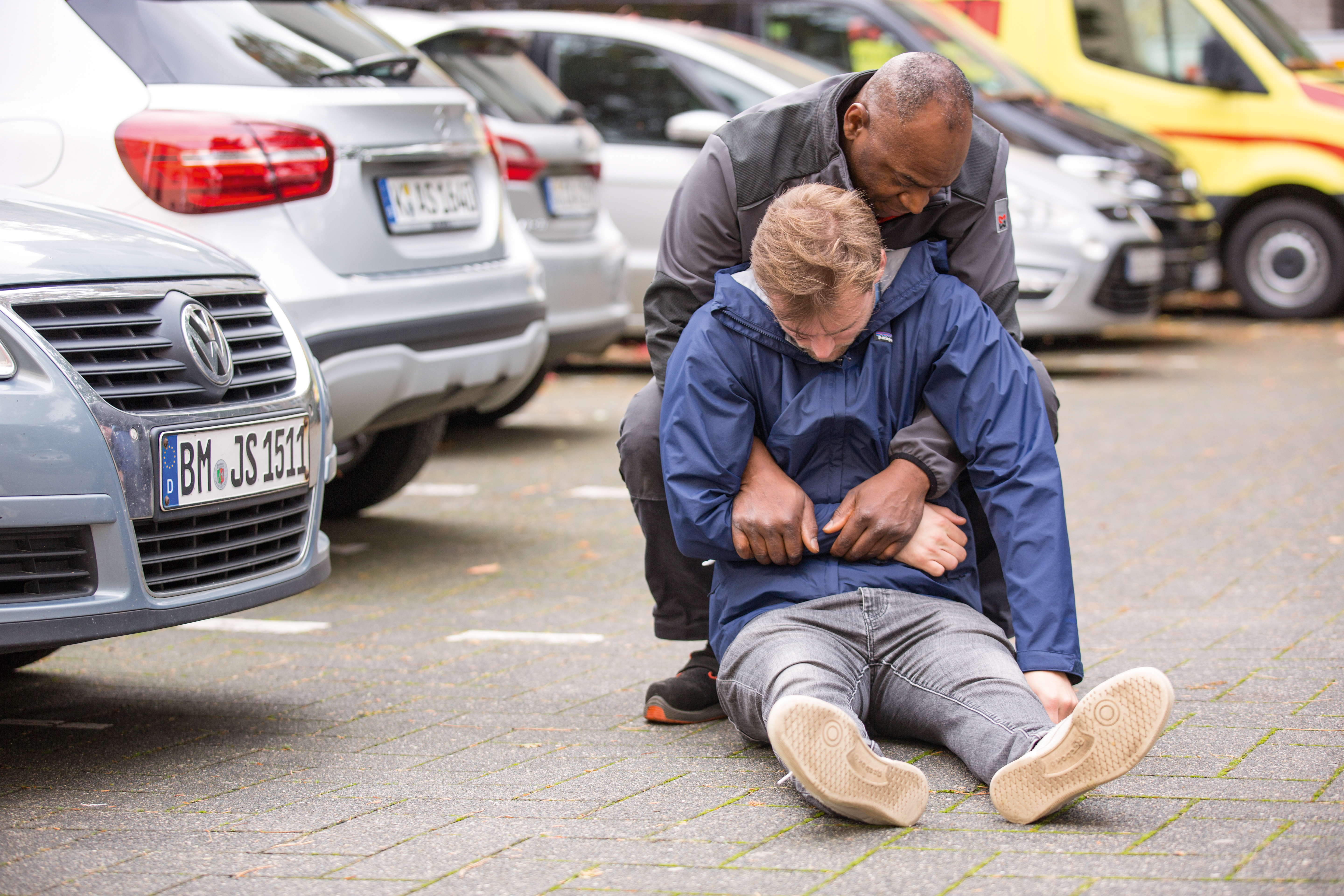Ein Mann leistet einem anderen Mann Erste-Hilfe und zieht ihn mit dem Rettungsgriff aus einer Gefahrensituation.
